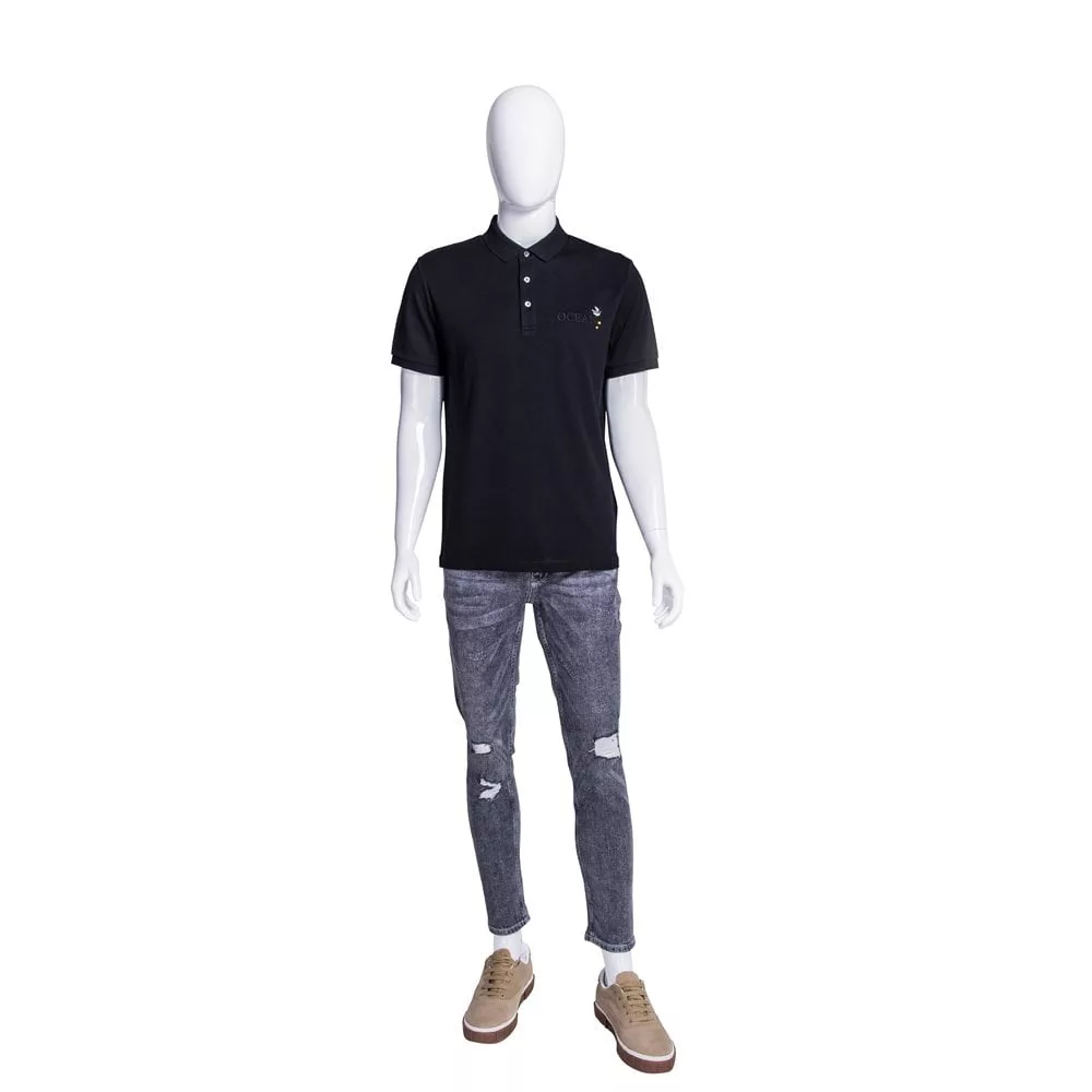 The Percy Plastic Gloss White Male Mannequin stands on a white background, dressed in a black polo shirt and distressed blue jeans with patches. Its light brown sneakers complement the ensemble, exuding casual style.