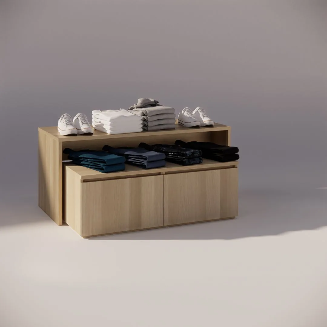 A wooden display unit holds neatly folded clothes, including stacked t-shirts in white, gray, black, and blue. White sneakers are placed on top. The setup is well-lit, casting soft shadows on the floor.